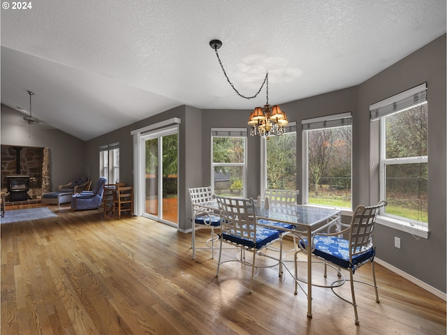 dining area with a textured ceiling, vaulted ceiling, wood-type flooring, a notable chandelier, and a wood stove