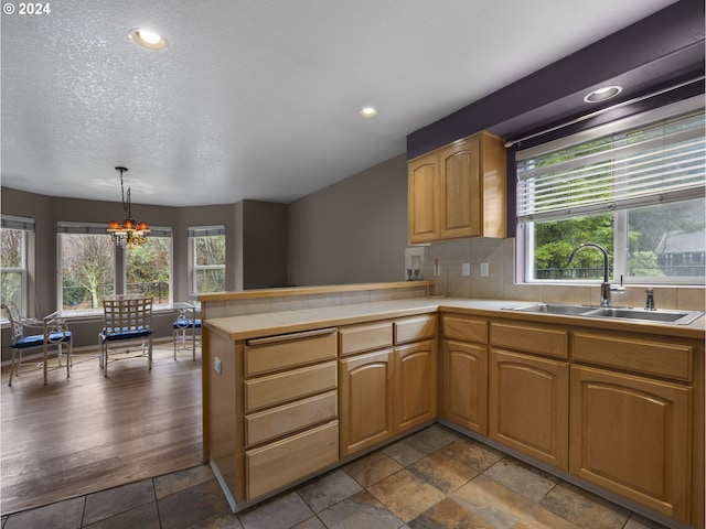 kitchen with sink, an inviting chandelier, tasteful backsplash, kitchen peninsula, and pendant lighting