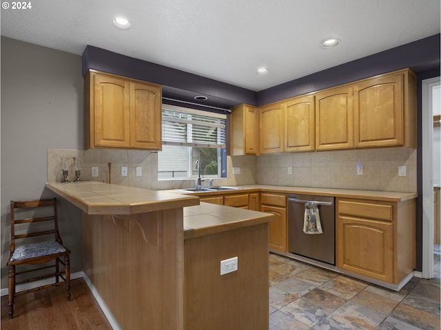 kitchen with tile counters, sink, stainless steel dishwasher, kitchen peninsula, and a breakfast bar