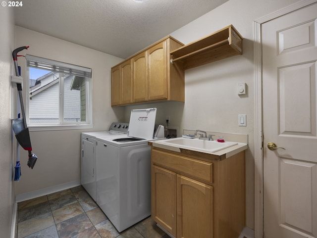 clothes washing area featuring washing machine and dryer, sink, cabinets, and a textured ceiling