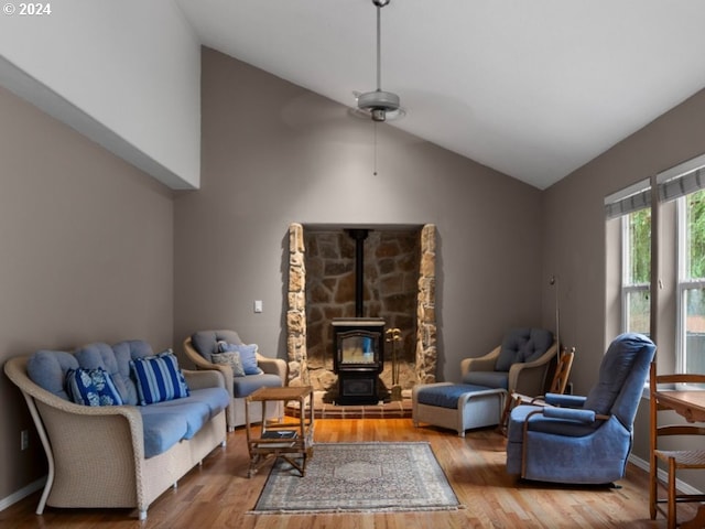 living room with hardwood / wood-style floors, vaulted ceiling, a wood stove, and ceiling fan