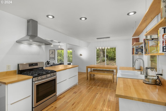 kitchen featuring sink, white cabinetry, butcher block counters, stainless steel range with gas cooktop, and wall chimney exhaust hood