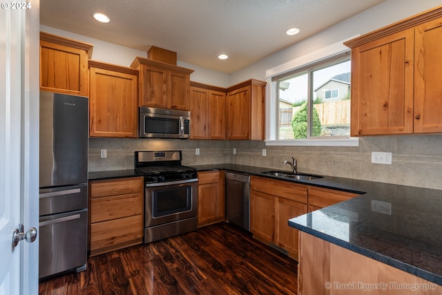 kitchen with stainless steel appliances, sink, dark stone counters, dark hardwood / wood-style floors, and backsplash