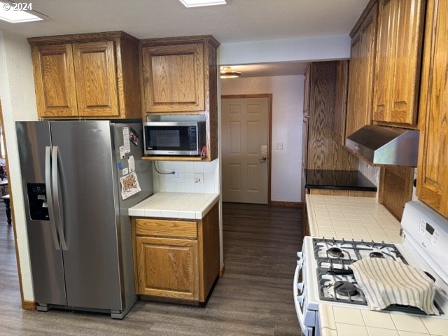 kitchen with tasteful backsplash, stainless steel appliances, tile counters, and dark hardwood / wood-style flooring