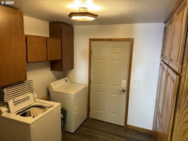 clothes washing area with cabinets, dark hardwood / wood-style flooring, washing machine and dryer, and a textured ceiling