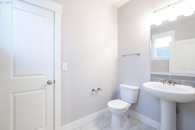 bathroom featuring tile patterned flooring, decorative backsplash, toilet, and sink