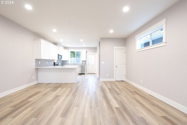 kitchen featuring kitchen peninsula, backsplash, stainless steel appliances, light hardwood / wood-style flooring, and white cabinets