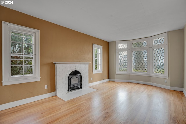 unfurnished living room featuring a wood stove, a wealth of natural light, and light hardwood / wood-style floors