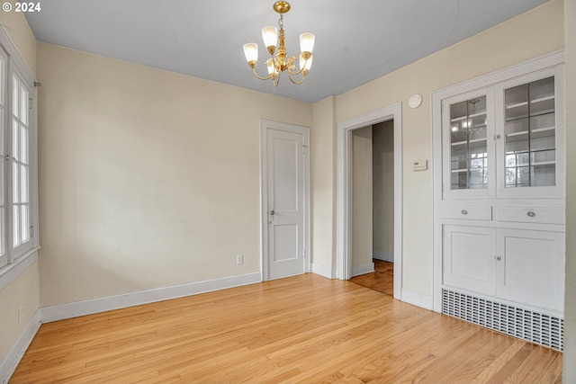 spare room with light hardwood / wood-style floors and an inviting chandelier