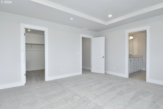 unfurnished bedroom with a closet, a spacious closet, light carpet, and ensuite bath