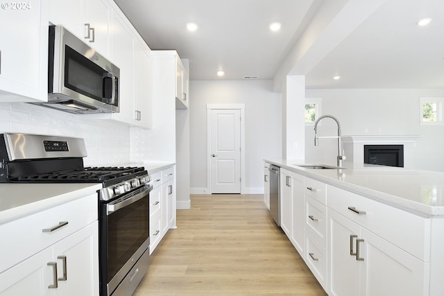 kitchen with appliances with stainless steel finishes, sink, a center island with sink, light hardwood / wood-style floors, and white cabinetry