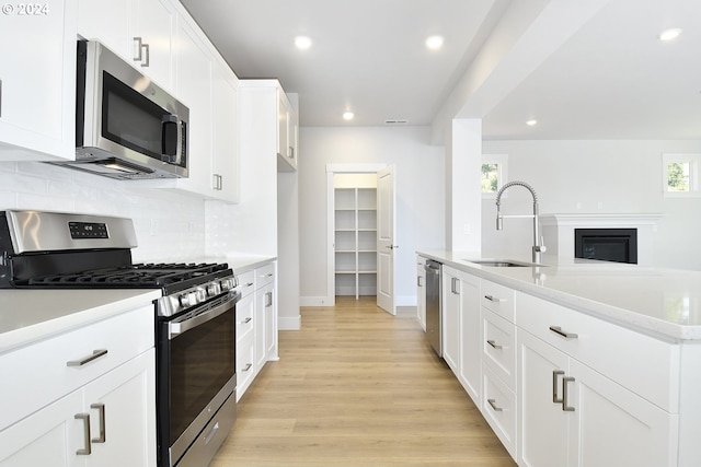 kitchen featuring sink, appliances with stainless steel finishes, a kitchen island with sink, white cabinets, and light wood-type flooring