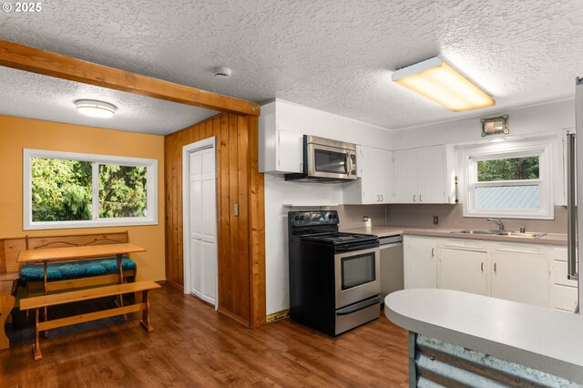 kitchen with wood walls, white cabinets, sink, hardwood / wood-style flooring, and appliances with stainless steel finishes