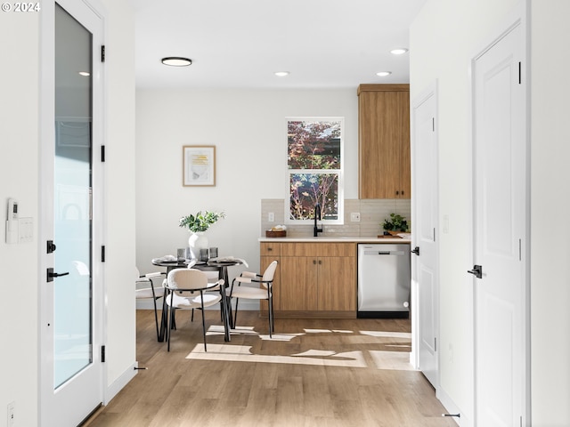 bar featuring stainless steel dishwasher, sink, light wood-type flooring, and decorative backsplash