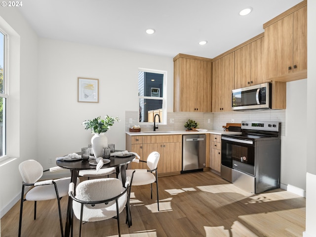 kitchen featuring stainless steel appliances, sink, tasteful backsplash, light hardwood / wood-style flooring, and light brown cabinetry