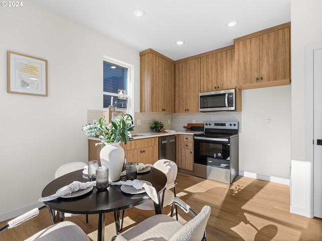 kitchen featuring stainless steel appliances, sink, backsplash, and light hardwood / wood-style flooring