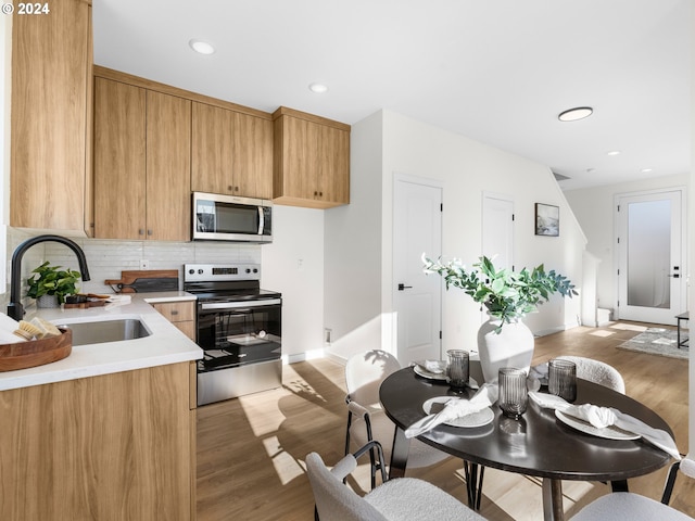 kitchen featuring decorative backsplash, light wood-type flooring, appliances with stainless steel finishes, and sink