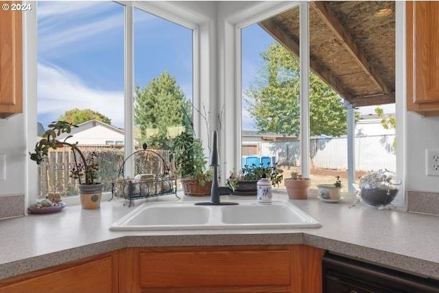 kitchen with brown cabinetry, a sink, dishwashing machine, and light countertops