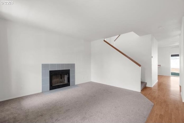 unfurnished living room featuring a fireplace, stairs, and wood finished floors