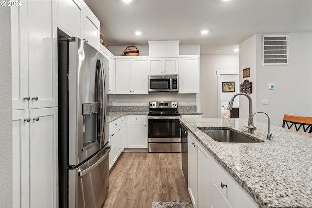 kitchen with sink, stainless steel appliances, light stone counters, light hardwood / wood-style floors, and white cabinets