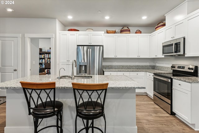 kitchen with light hardwood / wood-style floors, a kitchen bar, stainless steel appliances, and a kitchen island with sink