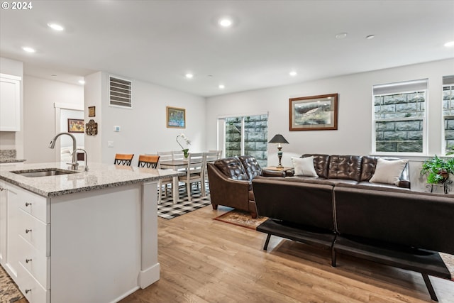 kitchen featuring white cabinetry, sink, light stone counters, a center island with sink, and light wood-type flooring