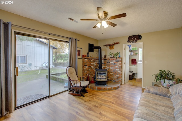 living room with a wood stove, ceiling fan, a textured ceiling, and light wood-type flooring