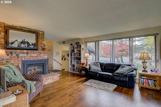 living room featuring hardwood / wood-style flooring, a textured ceiling, and a brick fireplace