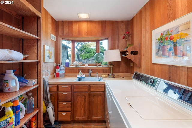 clothes washing area featuring independent washer and dryer, cabinets, sink, and wooden walls