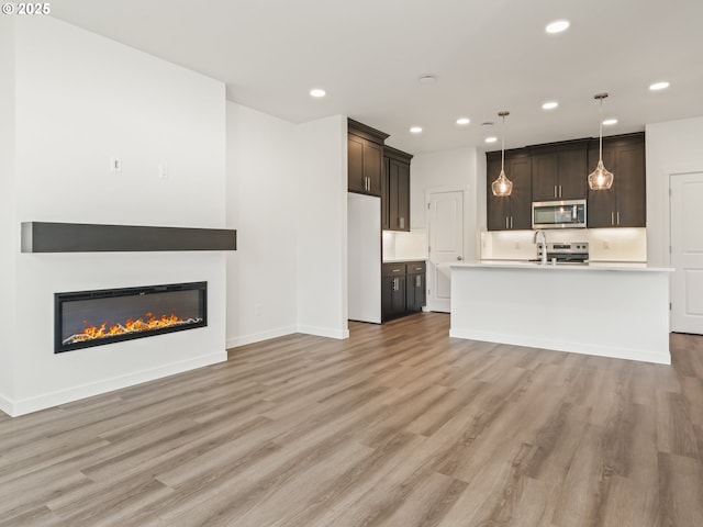 unfurnished living room featuring baseboards, light wood-type flooring, a glass covered fireplace, and recessed lighting