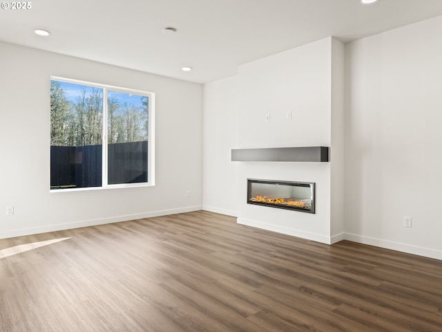 unfurnished living room featuring a glass covered fireplace, wood finished floors, and baseboards