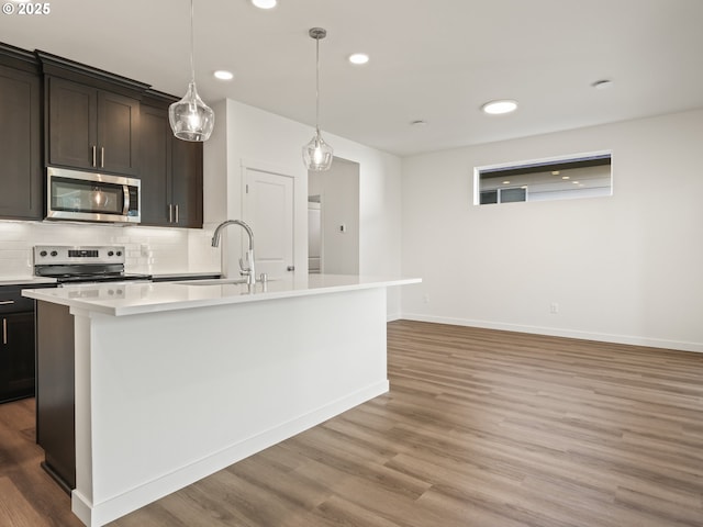 kitchen with an island with sink, light wood-style flooring, appliances with stainless steel finishes, light countertops, and backsplash