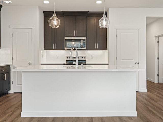 kitchen with dark wood-style flooring, a kitchen island with sink, stainless steel appliances, dark brown cabinets, and light countertops