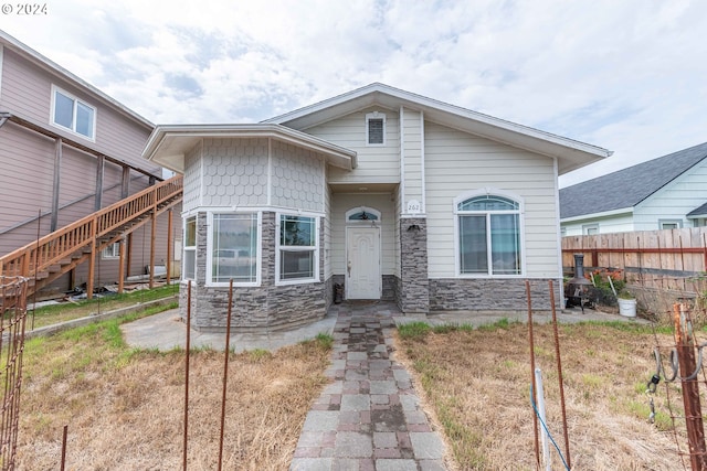 view of front facade featuring stone siding, stairway, and fence