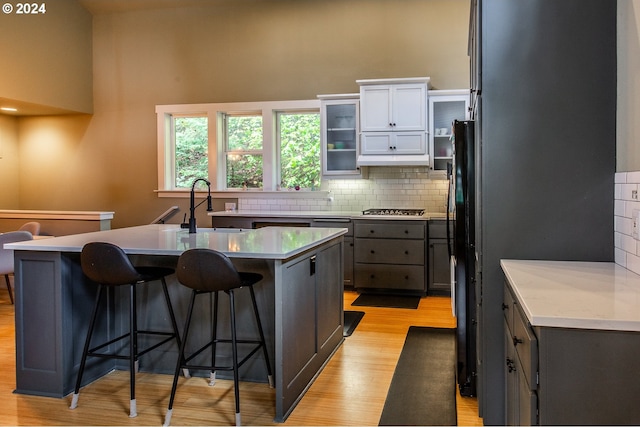 kitchen featuring a breakfast bar, white cabinetry, a center island with sink, and light wood-type flooring