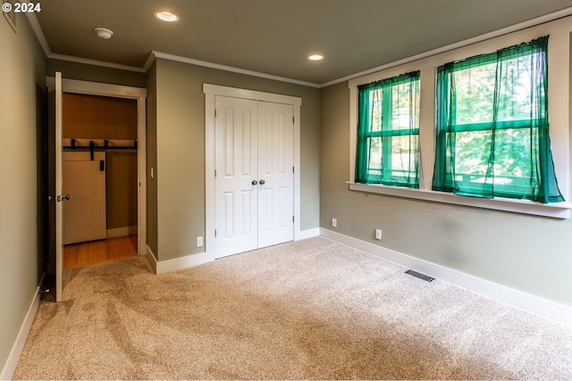 unfurnished bedroom with crown molding, a barn door, and carpet floors