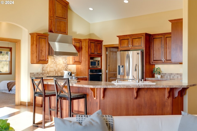 kitchen with stainless steel appliances, light countertops, wall chimney range hood, decorative backsplash, and a kitchen bar