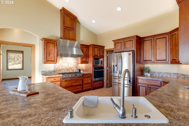 kitchen with decorative backsplash, high vaulted ceiling, stainless steel appliances, and wall chimney range hood