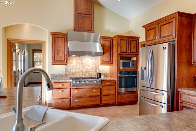 kitchen with sink, wall chimney exhaust hood, tasteful backsplash, lofted ceiling, and appliances with stainless steel finishes