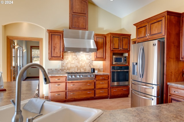 kitchen featuring stainless steel appliances, light countertops, backsplash, a sink, and wall chimney exhaust hood