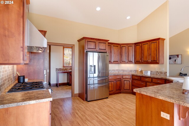 kitchen featuring high vaulted ceiling, wall chimney range hood, sink, light wood-type flooring, and stainless steel appliances