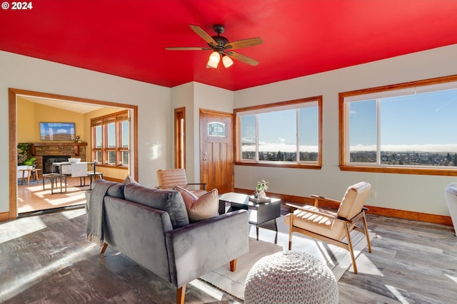 living area featuring light wood-style floors, baseboards, a ceiling fan, and a stone fireplace