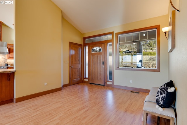 foyer entrance featuring light wood-style floors, visible vents, high vaulted ceiling, and baseboards