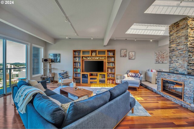 living room featuring beam ceiling, a stone fireplace, hardwood / wood-style floors, and rail lighting