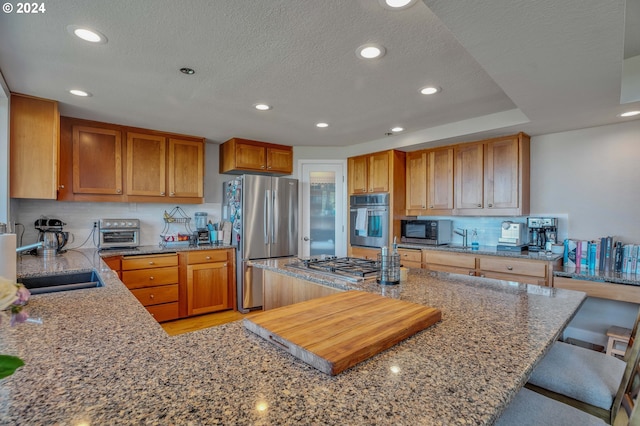 kitchen featuring a textured ceiling, appliances with stainless steel finishes, a kitchen breakfast bar, stone counters, and sink