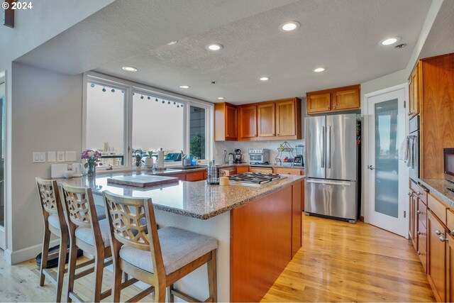 kitchen featuring appliances with stainless steel finishes, light hardwood / wood-style flooring, light stone counters, a kitchen breakfast bar, and a center island