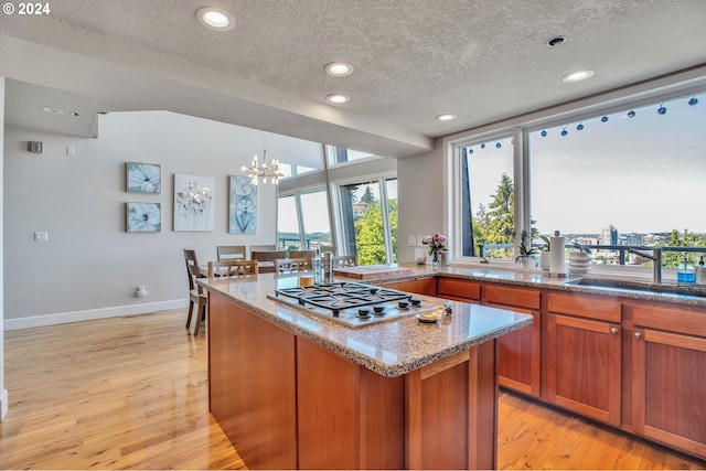 kitchen with stainless steel gas cooktop, decorative light fixtures, light hardwood / wood-style flooring, and a chandelier