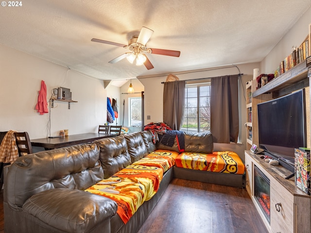 living room with a textured ceiling, ceiling fan, and dark wood-type flooring