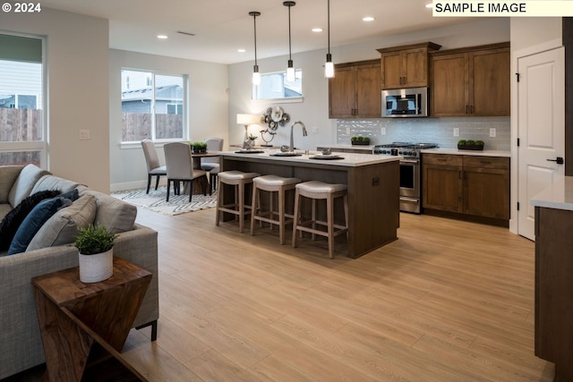 kitchen featuring a kitchen island with sink, light wood-type flooring, hanging light fixtures, and appliances with stainless steel finishes