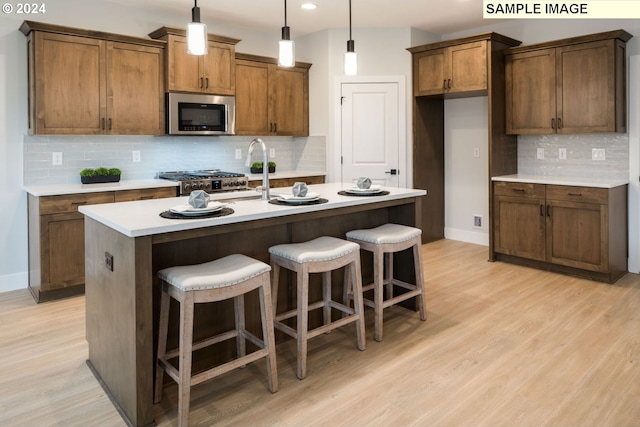 kitchen with appliances with stainless steel finishes, light wood-type flooring, tasteful backsplash, and a kitchen island with sink